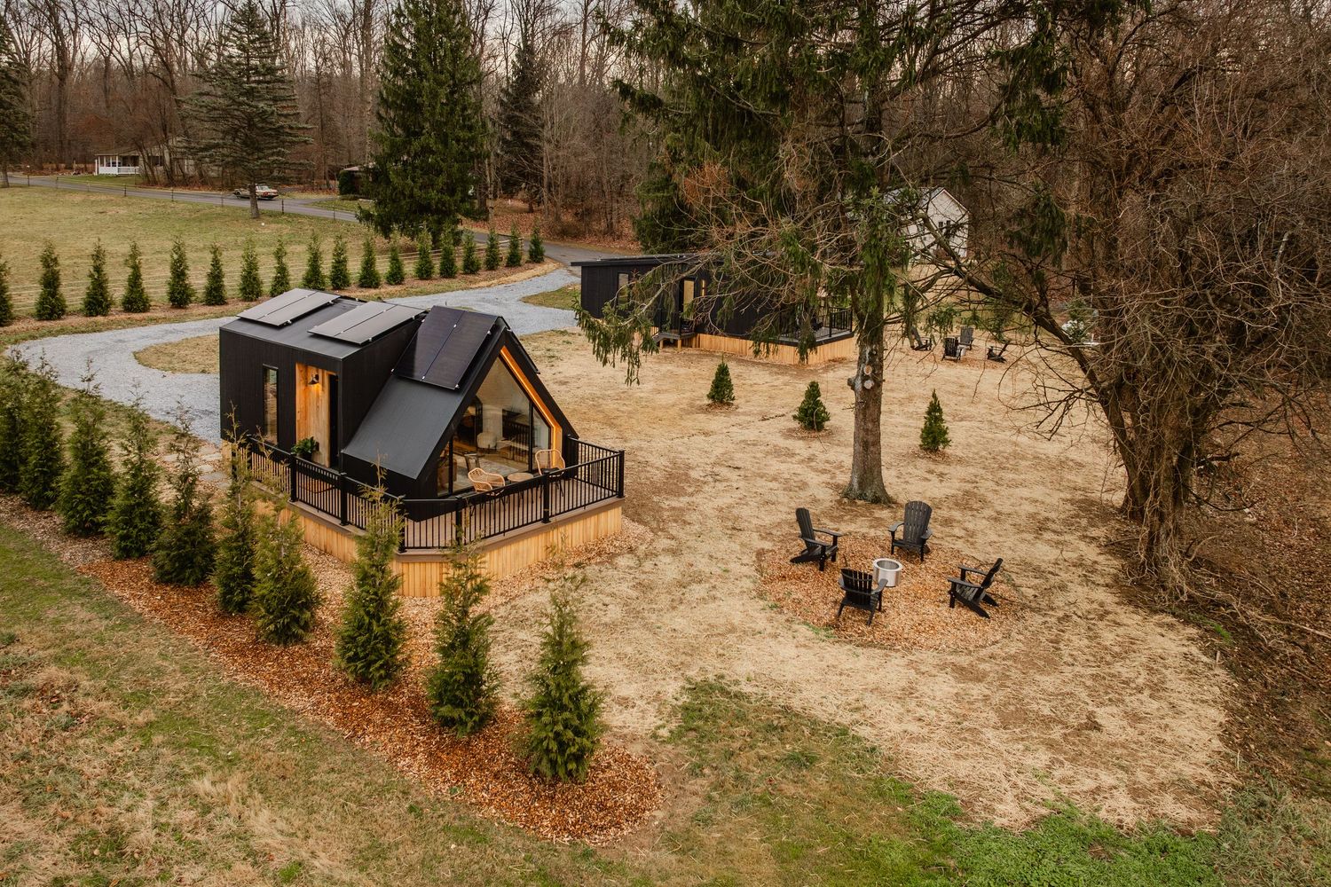 Aerial view of black A-frame cabins on a wooded property with a gravel driveway loop