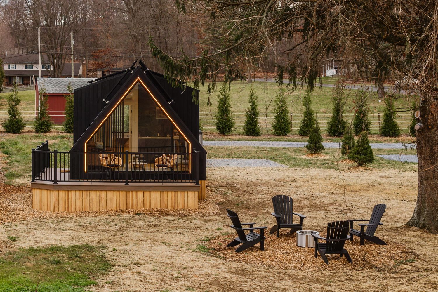 Aerial view of two black A-frame cabins tucked among bare trees with a fire pit clearing between them