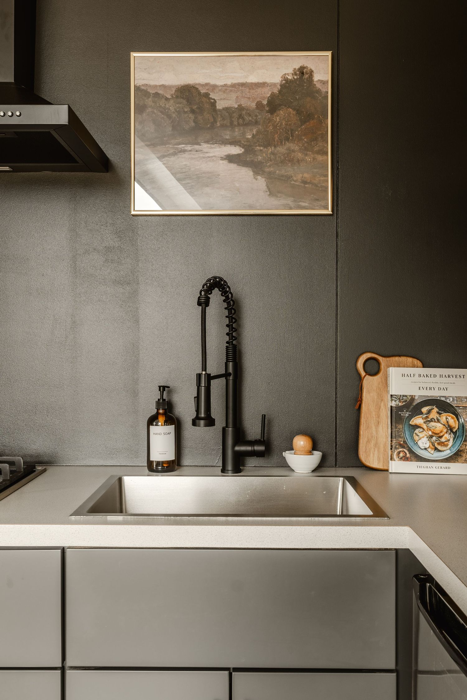 Dark moody kitchen nook with a matte black faucet, framed landscape art and floating shelf