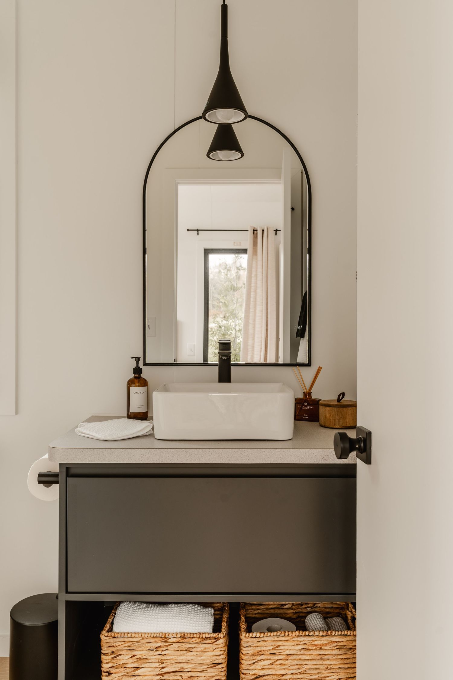 Bathroom vessel sink with an arched mirror, black pendant lights and a wood-look counter