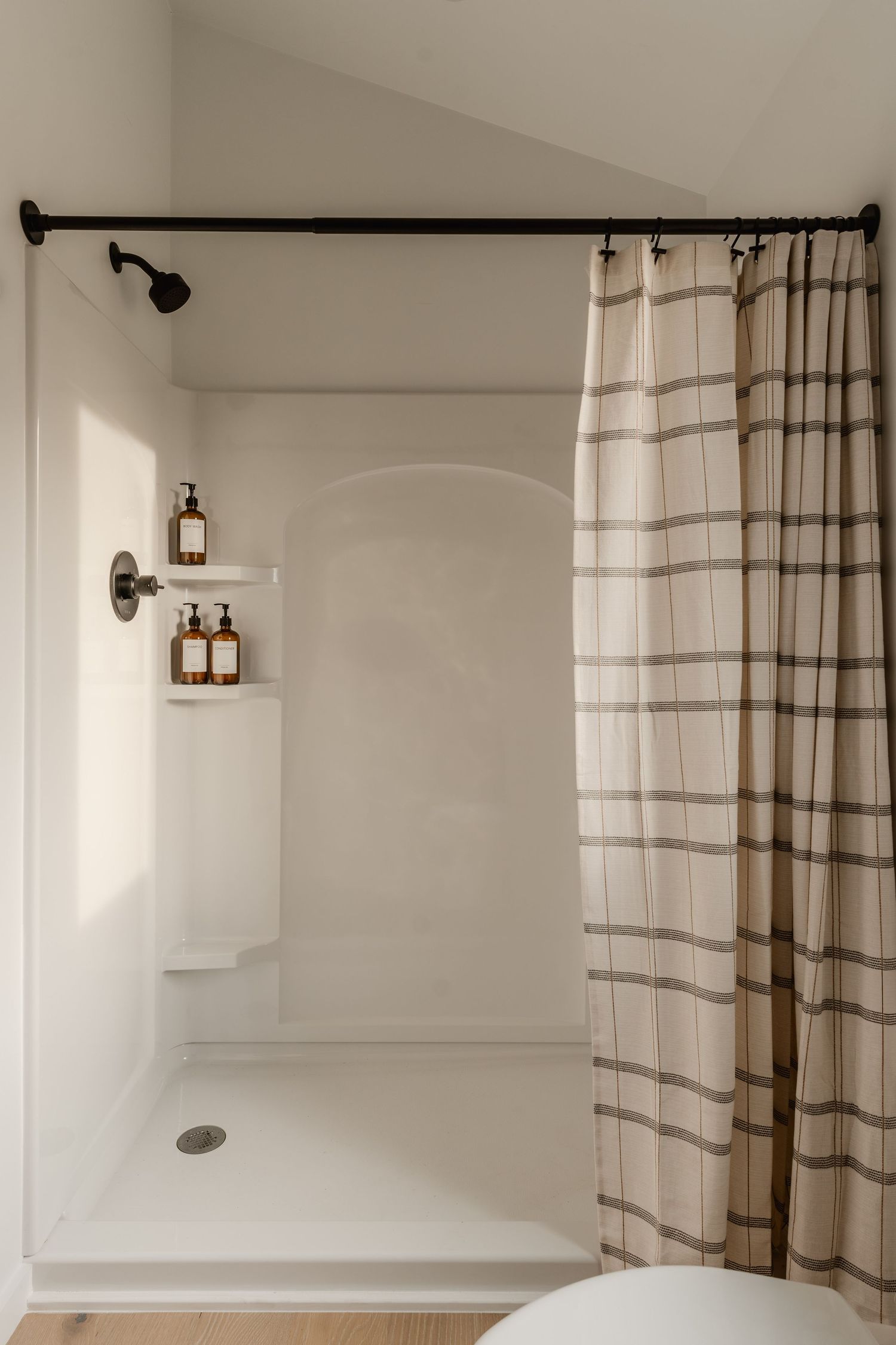 Walk-in shower with a plaid curtain, black fixtures and an arched tile niche