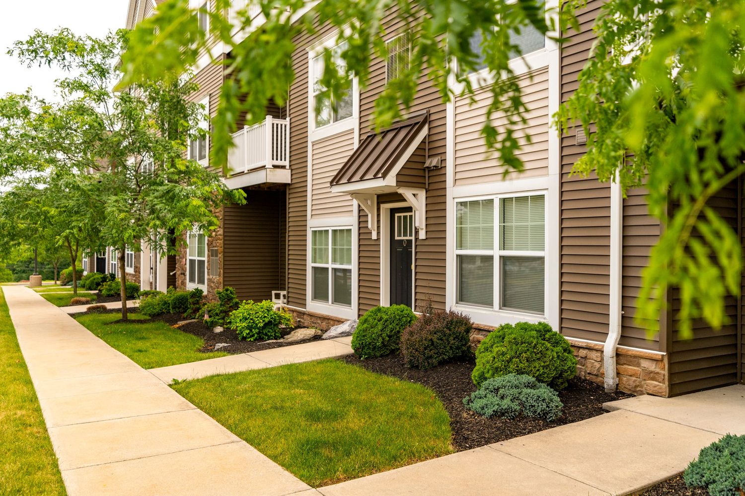 Apartment building exterior with brown siding, black door and mulched landscaping