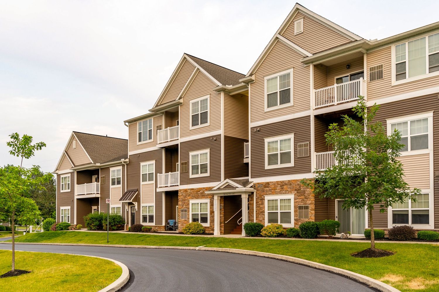 Apartment building exterior with tan and brown siding, a stone base and covered balconies