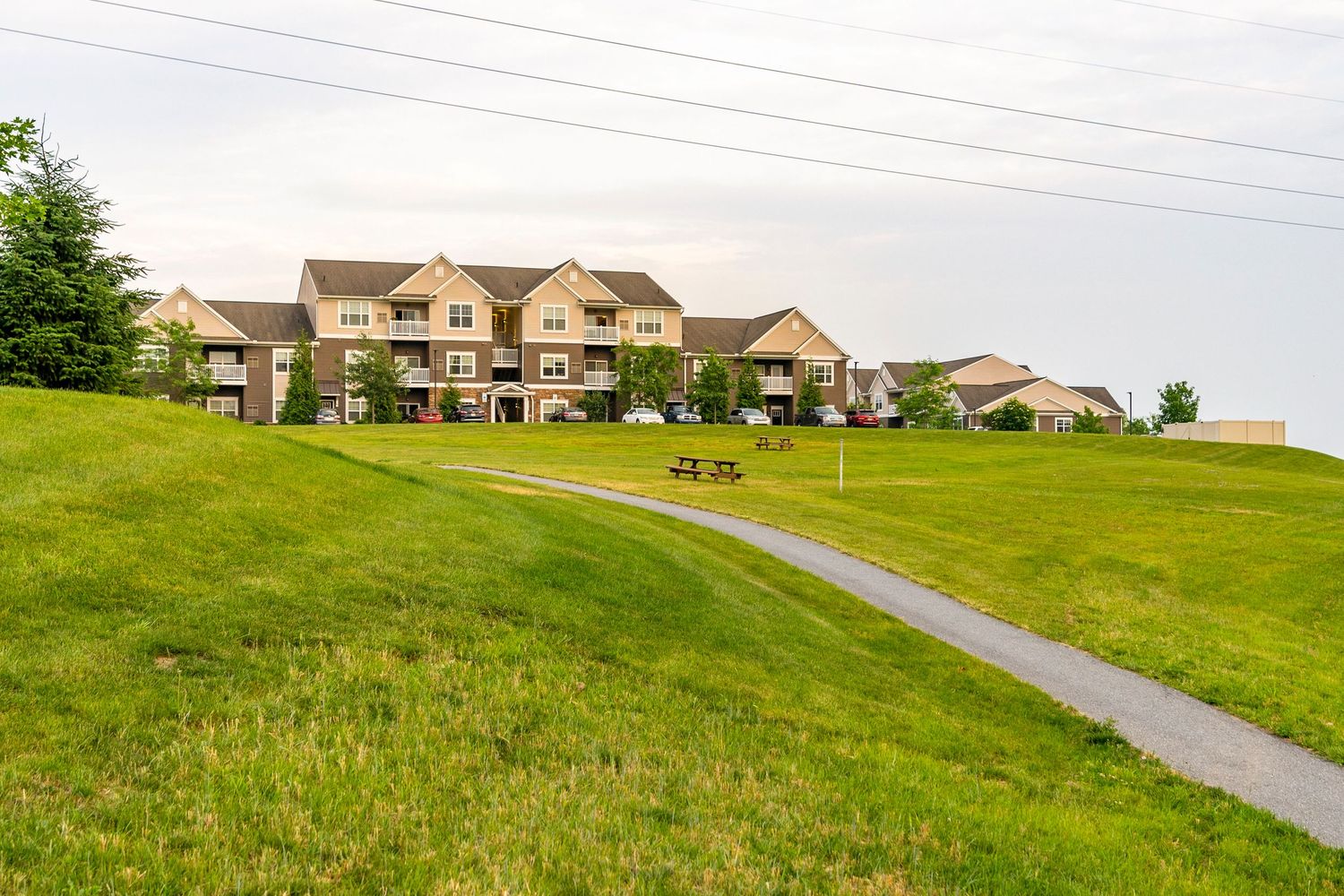 Aerial view of an apartment complex from a grassy hill with a walking path and picnic tables