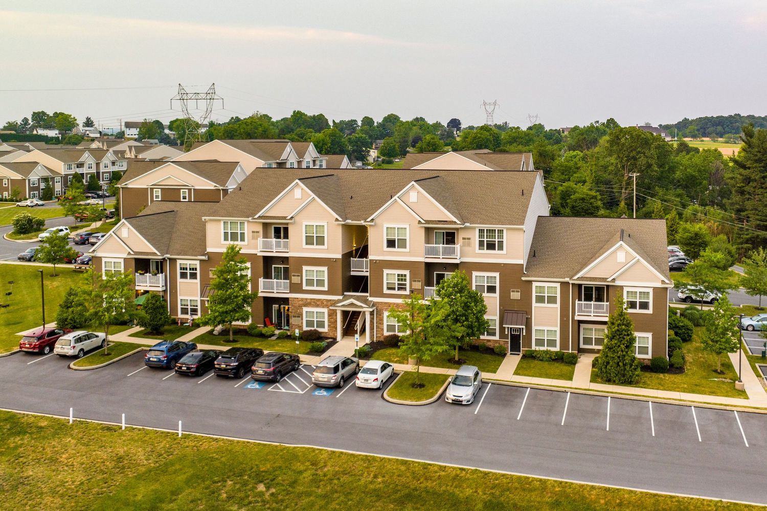 Aerial view of a three-story apartment building with balconies and a full parking lot