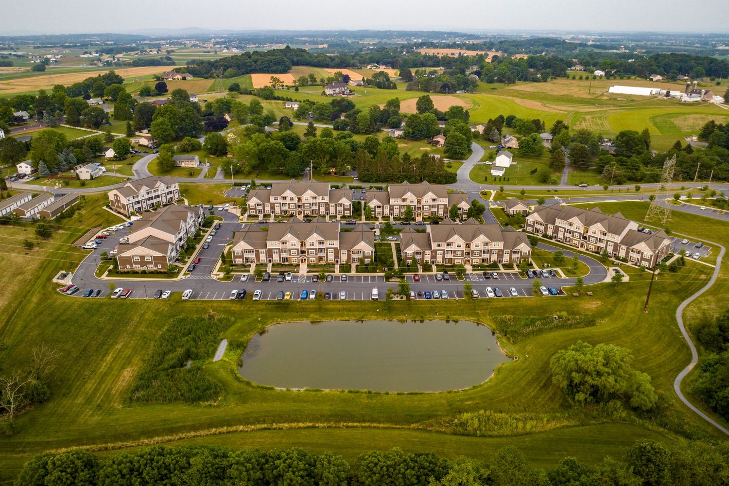 Aerial view of an apartment complex with a retention pond surrounded by farmland