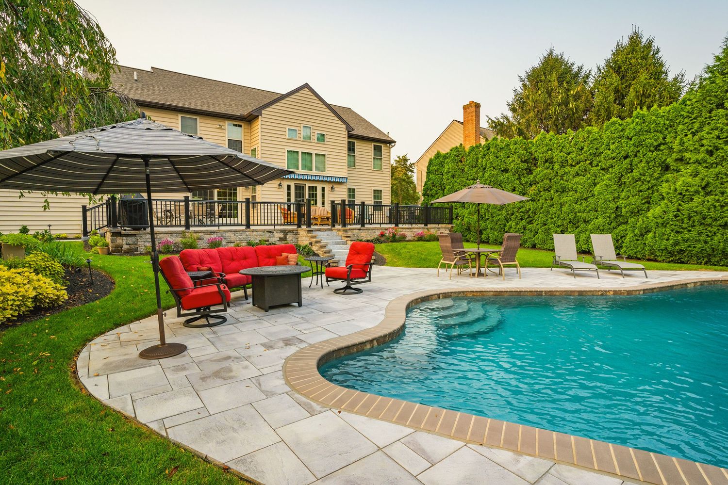 Backyard pool and paver patio with red furniture and a home at sunset