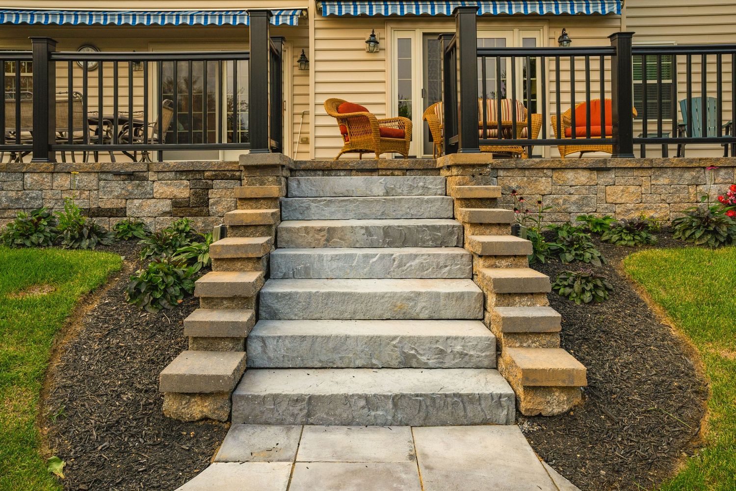 Stone steps leading up to a deck with wicker furniture and a stacked stone retaining wall