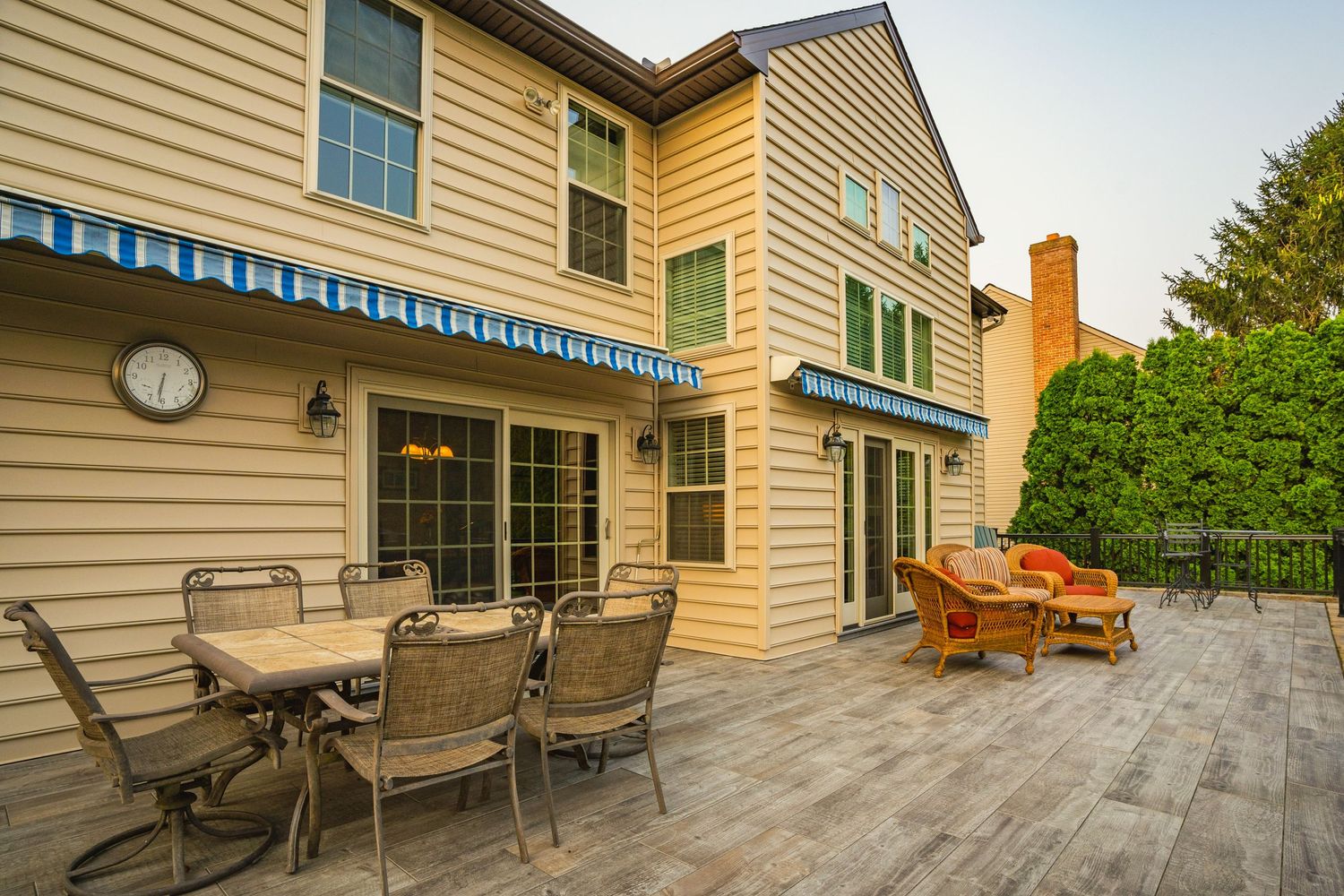 Composite deck with a dining table, wicker seating and a wall clock on the home's siding