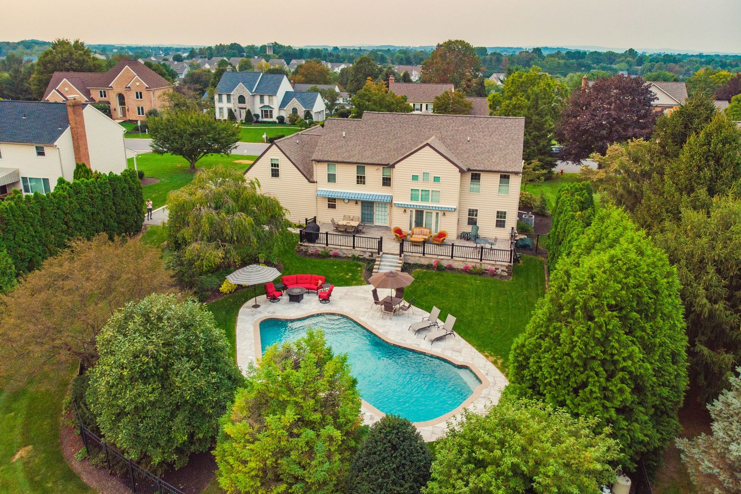 Aerial daytime view of a tan home's pool and deck backing up to a hazy suburban neighborhood