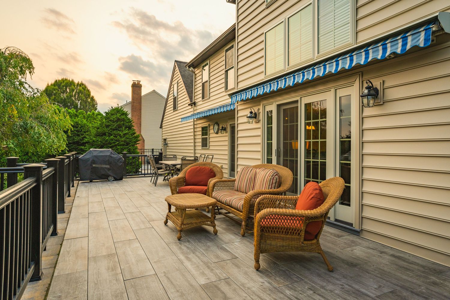 Composite deck with wicker patio furniture, a grill and a home at dusk