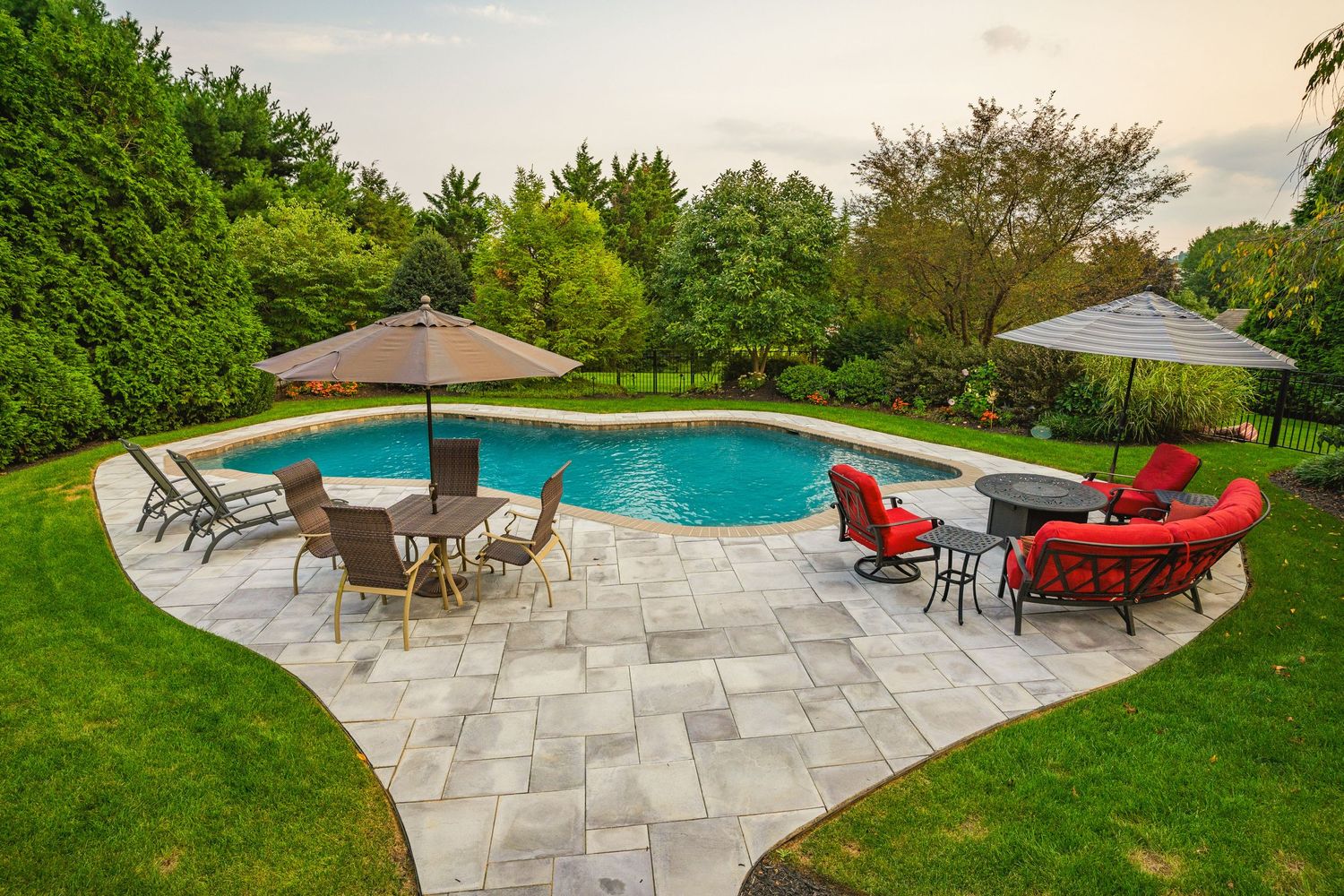 Backyard pool patio with red and wicker furniture, umbrellas and mature landscaping