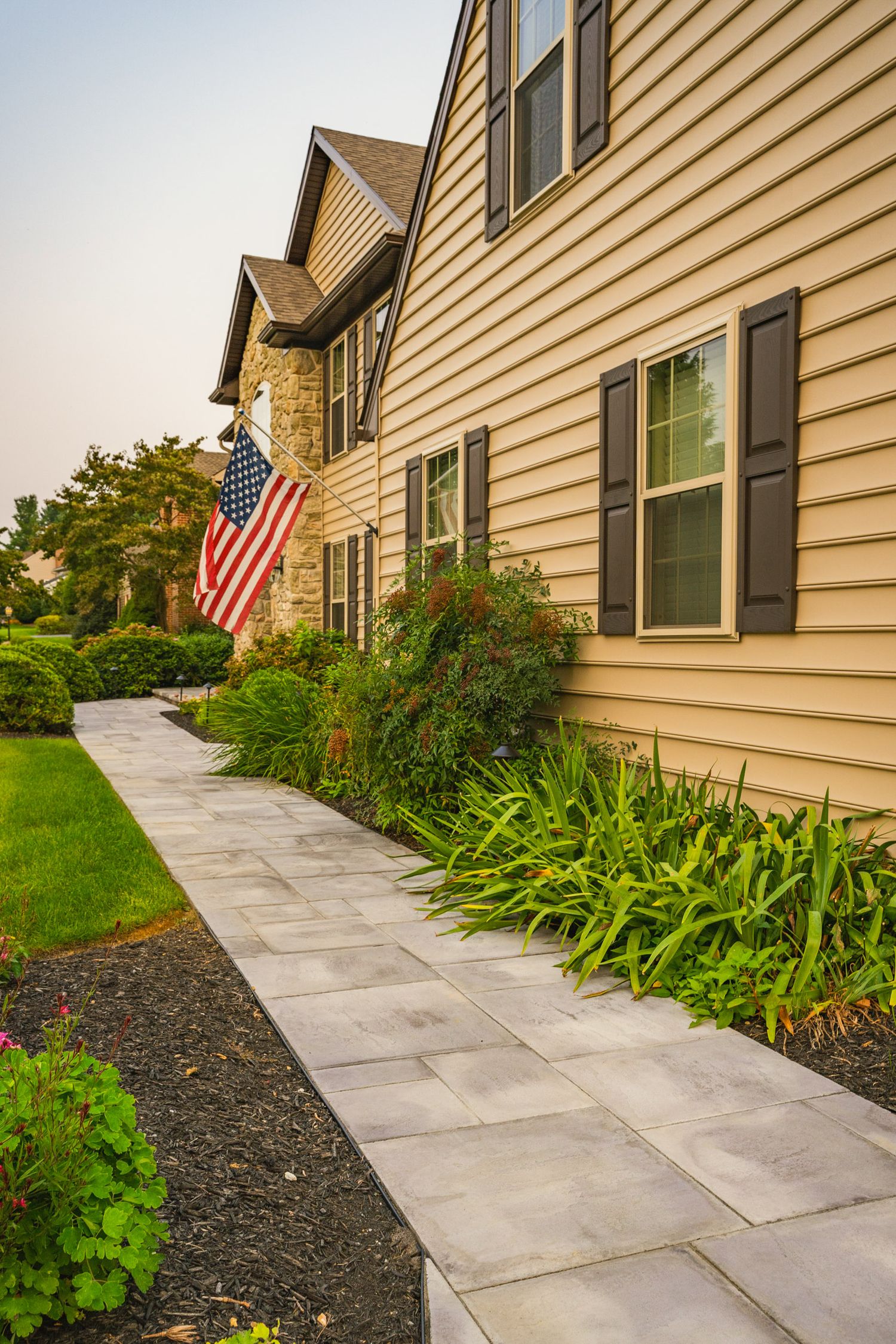Paver walkway along the side of a home with landscape beds and an American flag