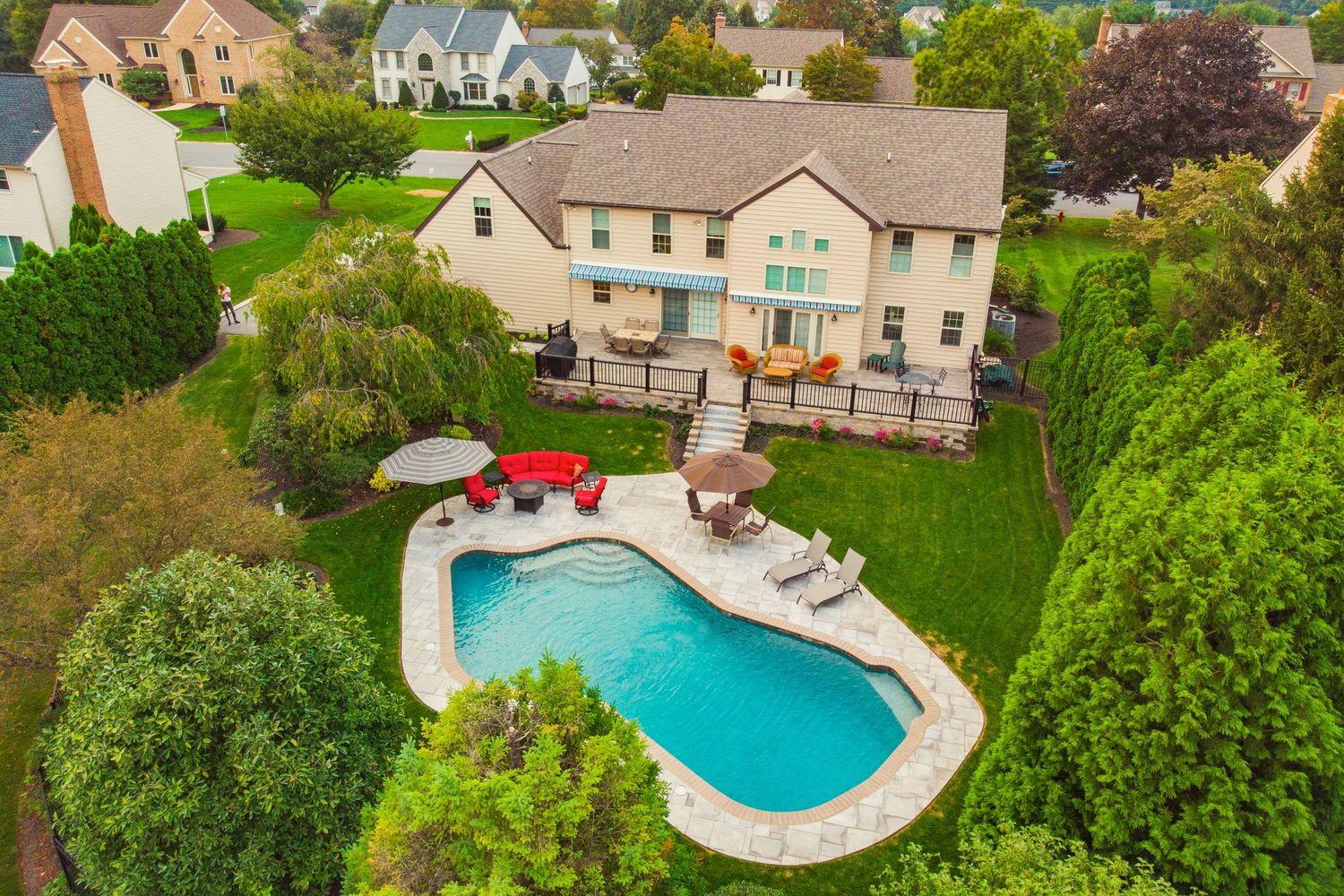 Aerial view of a tan two-story home, covered deck and free-form pool at golden hour with homes beyond