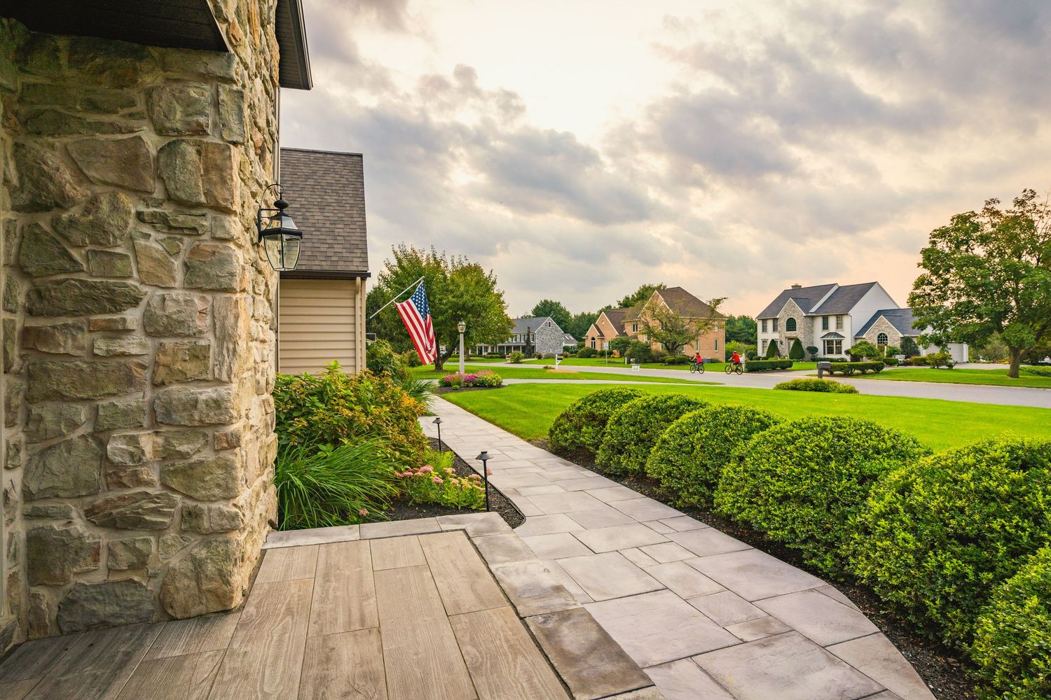 Paver front walkway leading to a stone-front porch in a manicured neighborhood