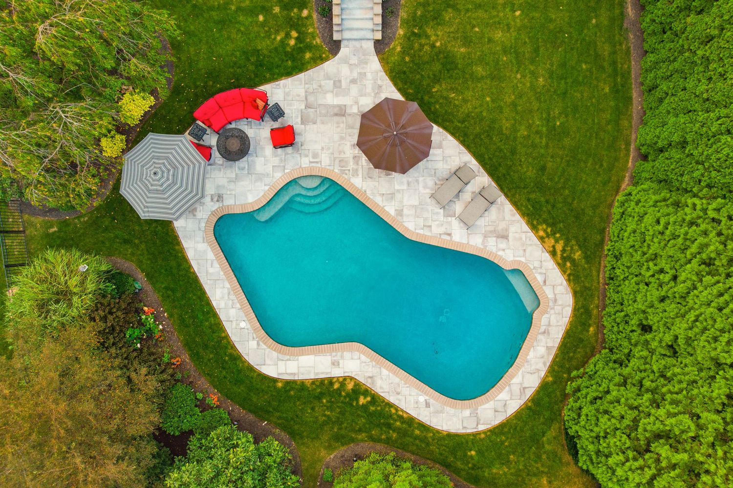 Top-down aerial view of a free-form pool with red outdoor seating, umbrellas and lounge chairs