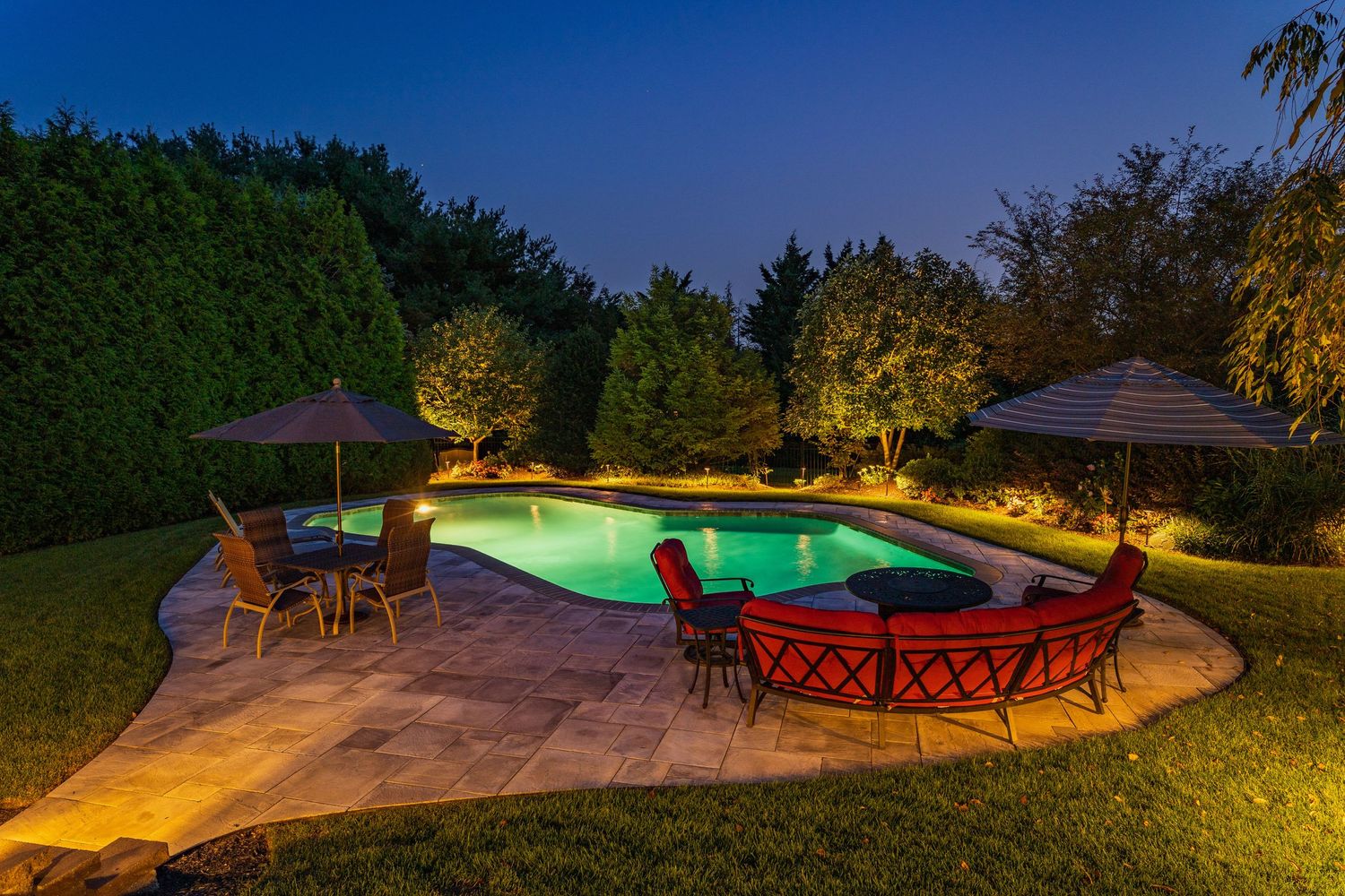Poolside patio at dusk with a red sectional, fire table and string of umbrellas