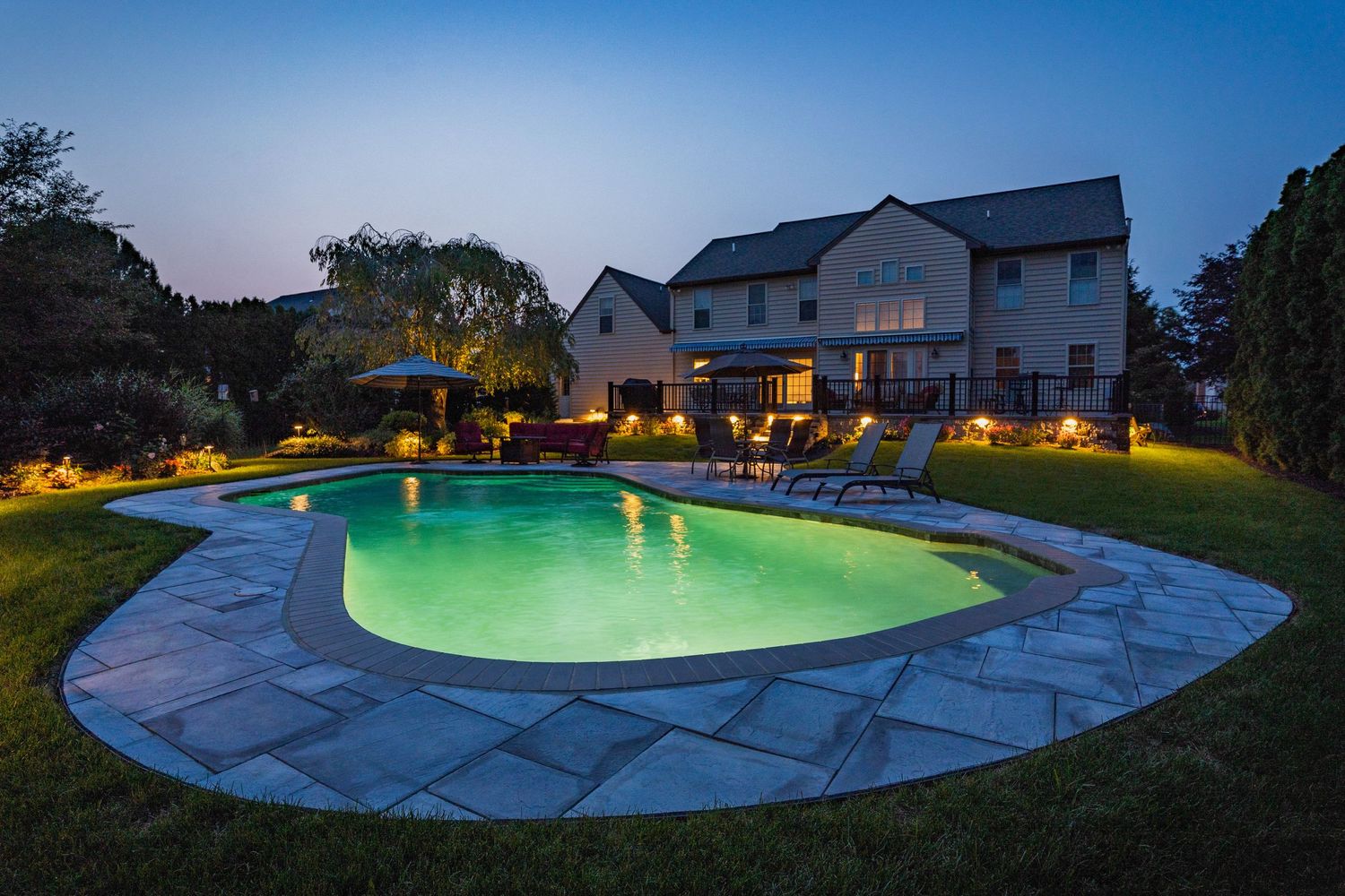 Backyard pool lit green at dusk with a paver patio and outdoor dining set