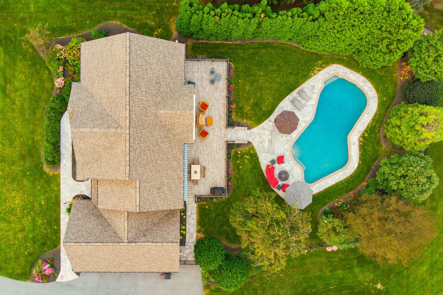 Aerial view of a home's rooftop and deck with a lounge and dining set beside a free-form pool
