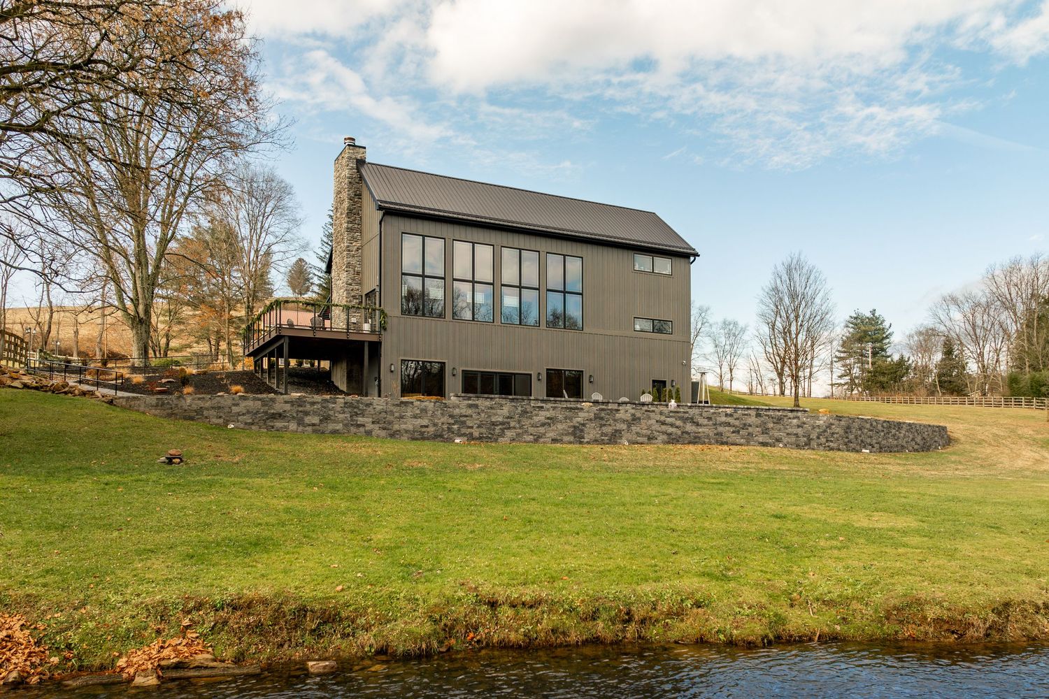 Grassy backyard bordered by a creek with a stone retaining wall and farmhouse in the distance