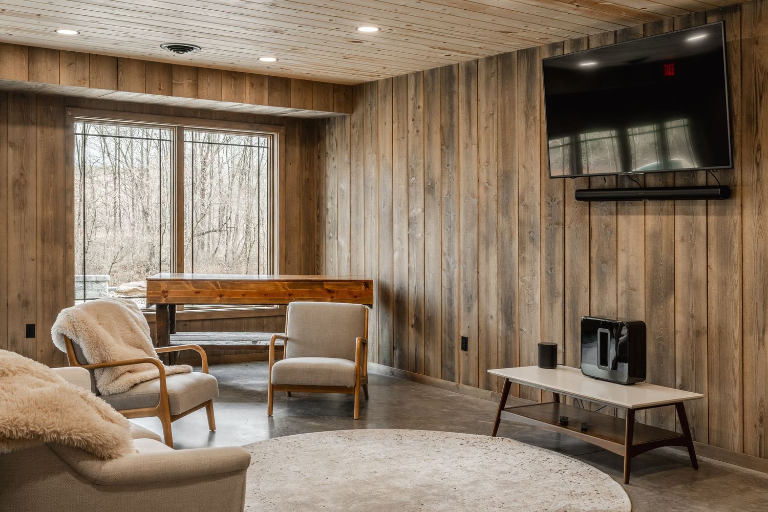 Cozy wood-paneled lounge nook with armchairs, mounted TV and a round area rug
