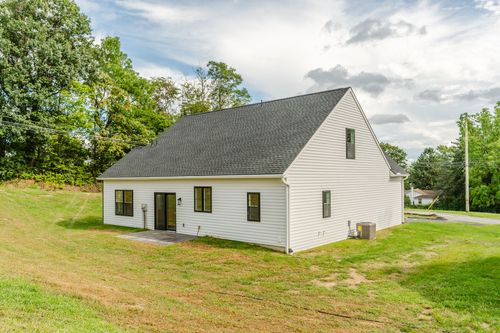 Side exterior of a steep-roofed white home with black windows, patio and an outdoor unit