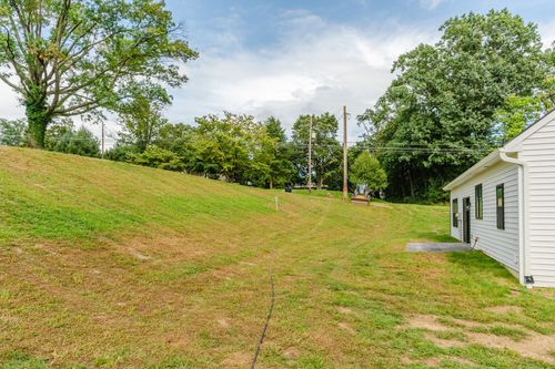 Grassy sloped side yard bordered by trees on a new-construction lot