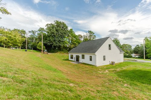 Side elevation of a white cape-style home with black windows on a sloped lawn