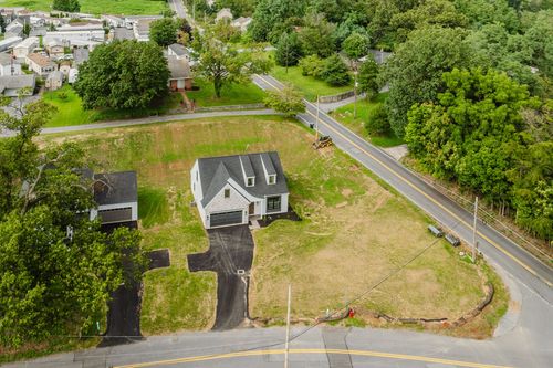 Aerial view of a gray and white two-story home with a black garage door on a wooded lot