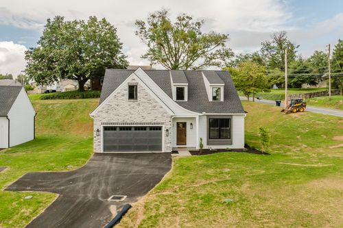 Aerial view of a new stone-and-white two-story home with a paved driveway and landscaping equipment nearby