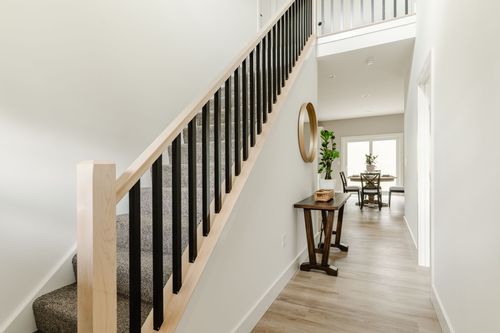 Foyer with a wood-and-black stair railing, round mirror and dark wood console table