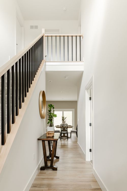 Two-story entry hall with black stair railing, round mirror and hardwood floors