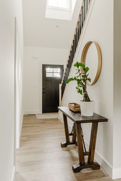 Entryway with a dark wood front door, staircase and round mirror over a console table