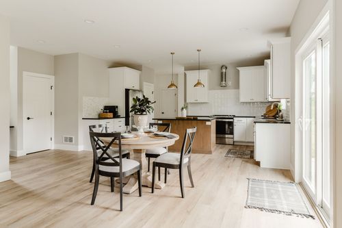 Open kitchen and dining area with a round table, white cabinets and a black range hood