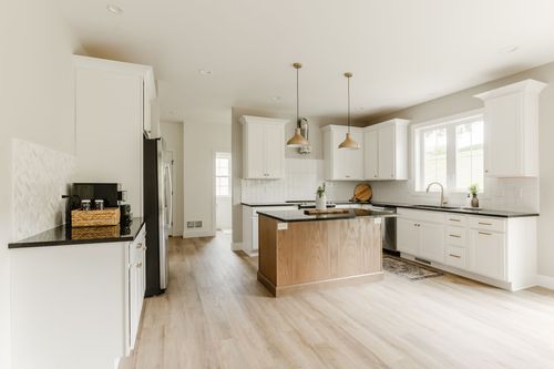 White kitchen with gold pendant lighting, black hardware and light hardwood floors