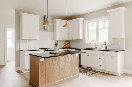 White kitchen with black countertops, a wood island base and gold pendant lights