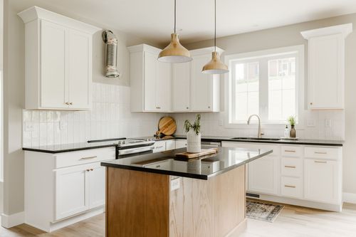 Kitchen island with a black countertop and gold pendant lighting over white cabinetry