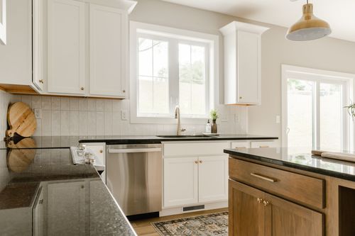 White kitchen with black granite counters, a stainless dishwasher and a window over the sink