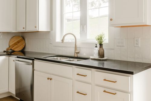 Kitchen sink with black granite counters, a gold faucet and a window view