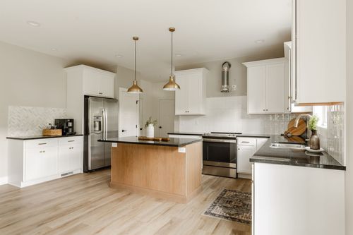 White kitchen with a stainless steel refrigerator, wood island and gold pendant lighting