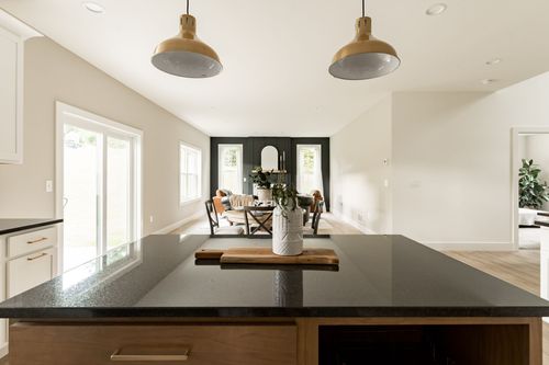 Black granite kitchen island counter with gold pendant lights and a dining area beyond