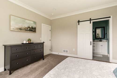 Bedroom with a dark wood dresser, framed art and a barn door leading to the ensuite bath