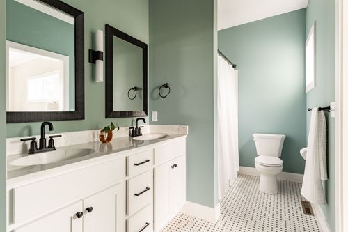 Sage green bathroom with white subway tile floor, double vanity and separate toilet area