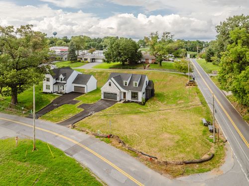 Aerial view of a new home and neighboring farmhouse along a country road with a water tower in the distance