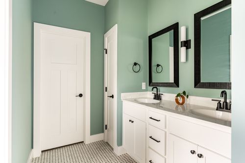 Sage green bathroom with double sinks, black mirrors and patterned tile flooring