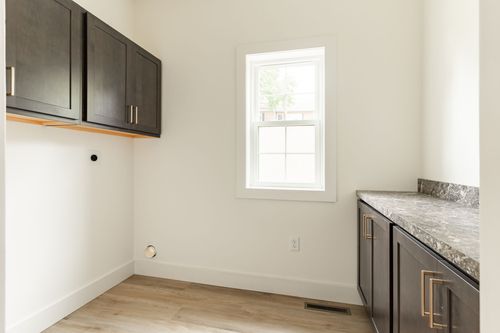 Laundry room with dark upper cabinets and a window above the hookup space