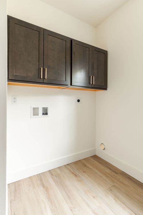 Laundry room with mounted dark cabinets above utility hookups