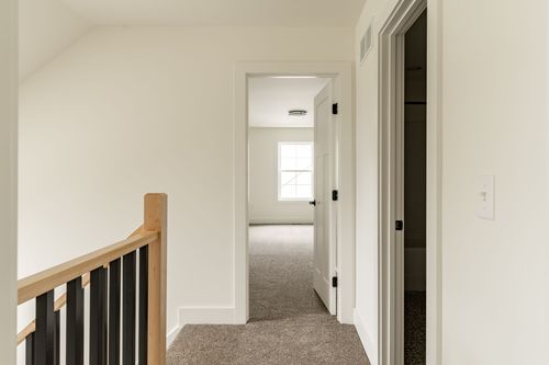 Upstairs hallway with carpet flooring and a black stair railing