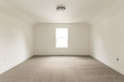 Empty carpeted bedroom with a single window and vaulted ceiling