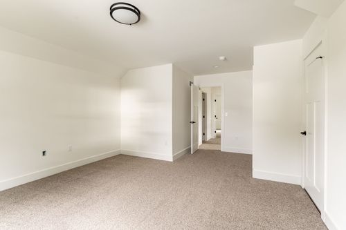 Empty carpeted bedroom with a vaulted ceiling and hallway view to a bathroom